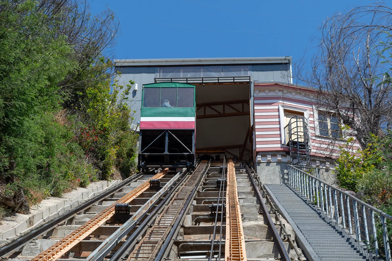 Carro vermelho e verde do Ascensor El Peral parado na estação, sobre os trilhos do funicular que sobe ao Cerro Alegre em Valparaíso