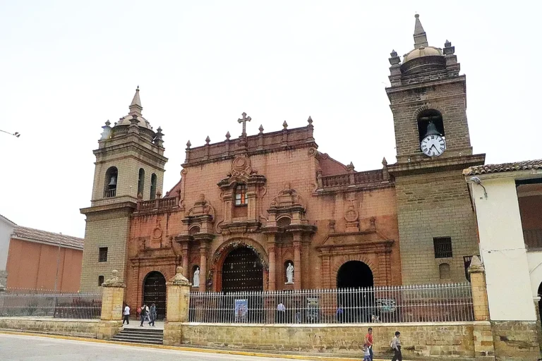 Fachada de pedra rosada da Catedral Basílica de Ayacucho, com duas torres e relógio, em frente à Plaza Mayor de Huamanga
