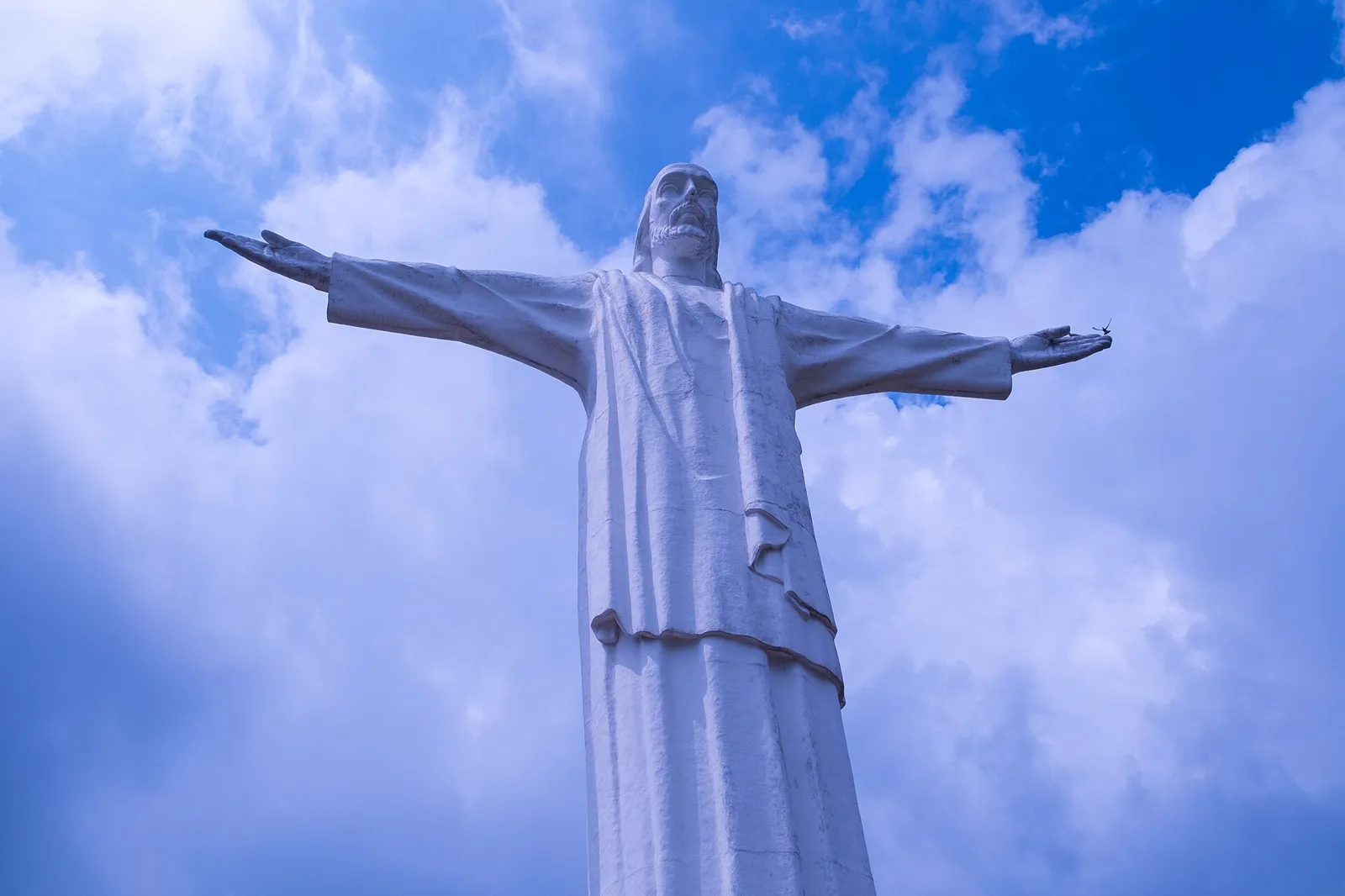 Estátua de Cristo Rey de braços abertos contra o céu azul, no Cerro de los Cristales, mirante de Cali