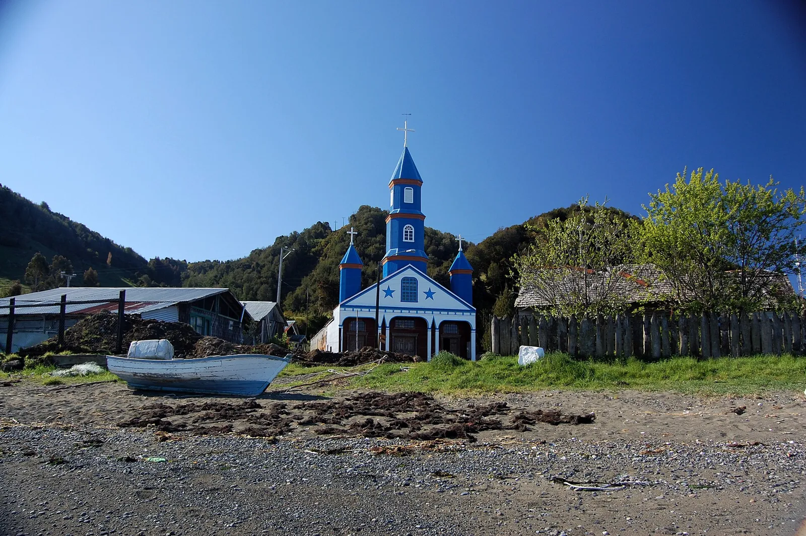 Igreja de Tenaún, em Chiloé, pintada de azul e branco com três torres, vista da praia com barcos de pesca