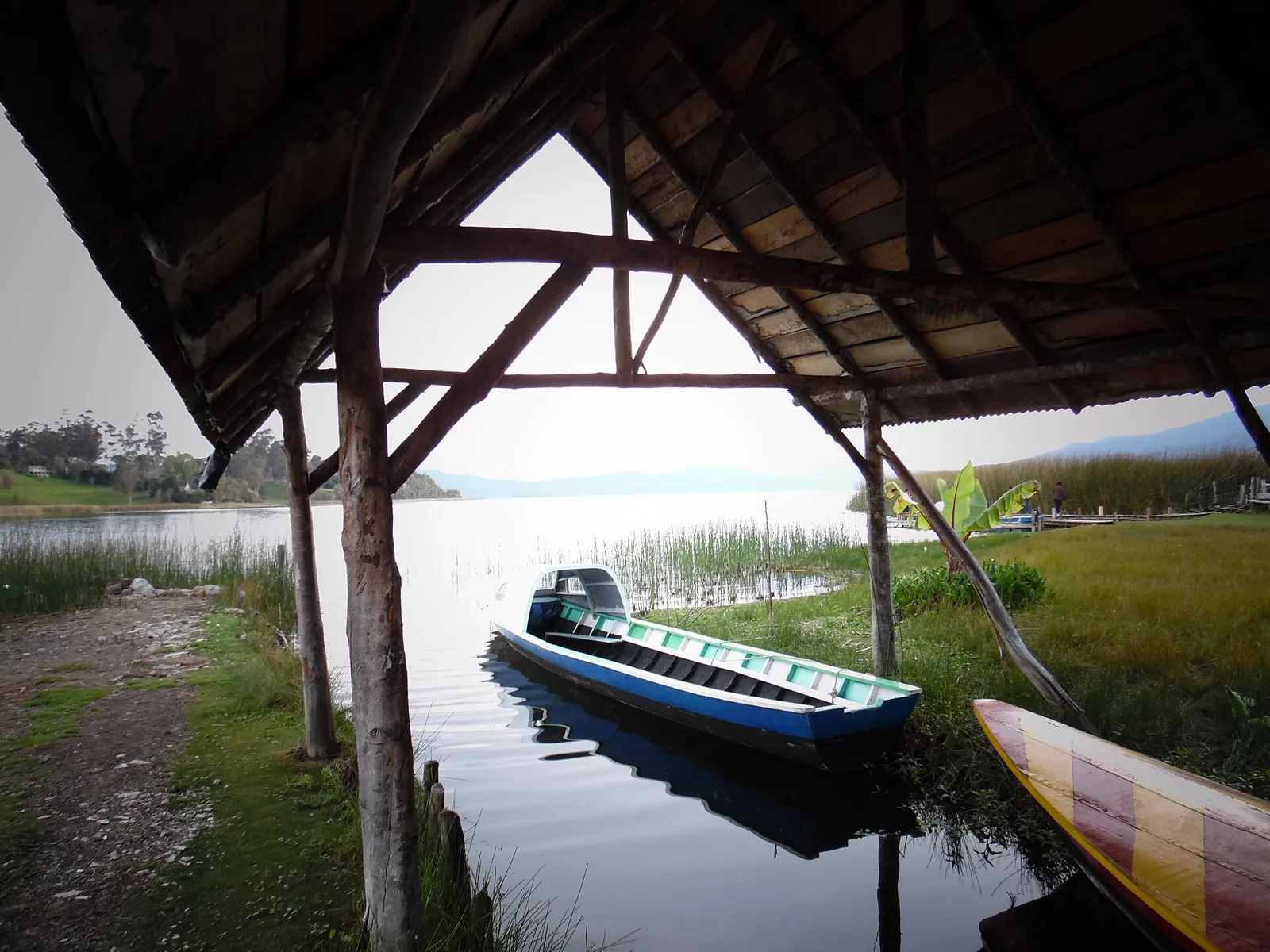 Barco atracado sob um cais coberto de madeira na Laguna de la Cocha, perto de Pasto, com totorais e montanhas ao fundo
