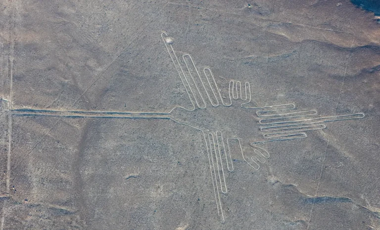 Vista aérea do geoglifo do beija-flor nas Linhas de Nazca, com bico longo e asas abertas desenhados em linhas claras sobre o deserto pedregoso