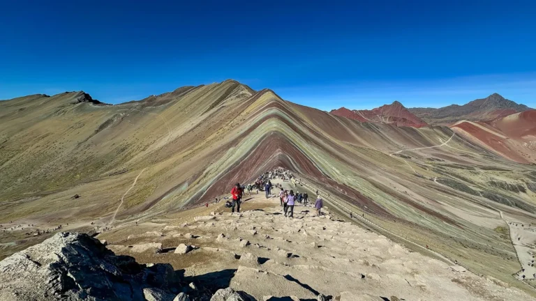 Trilha de pedra até o mirante da Montanha Colorida de Vinicunca, com faixas vermelhas, verdes e amarelas na encosta e o Valle Rojo ao fundo