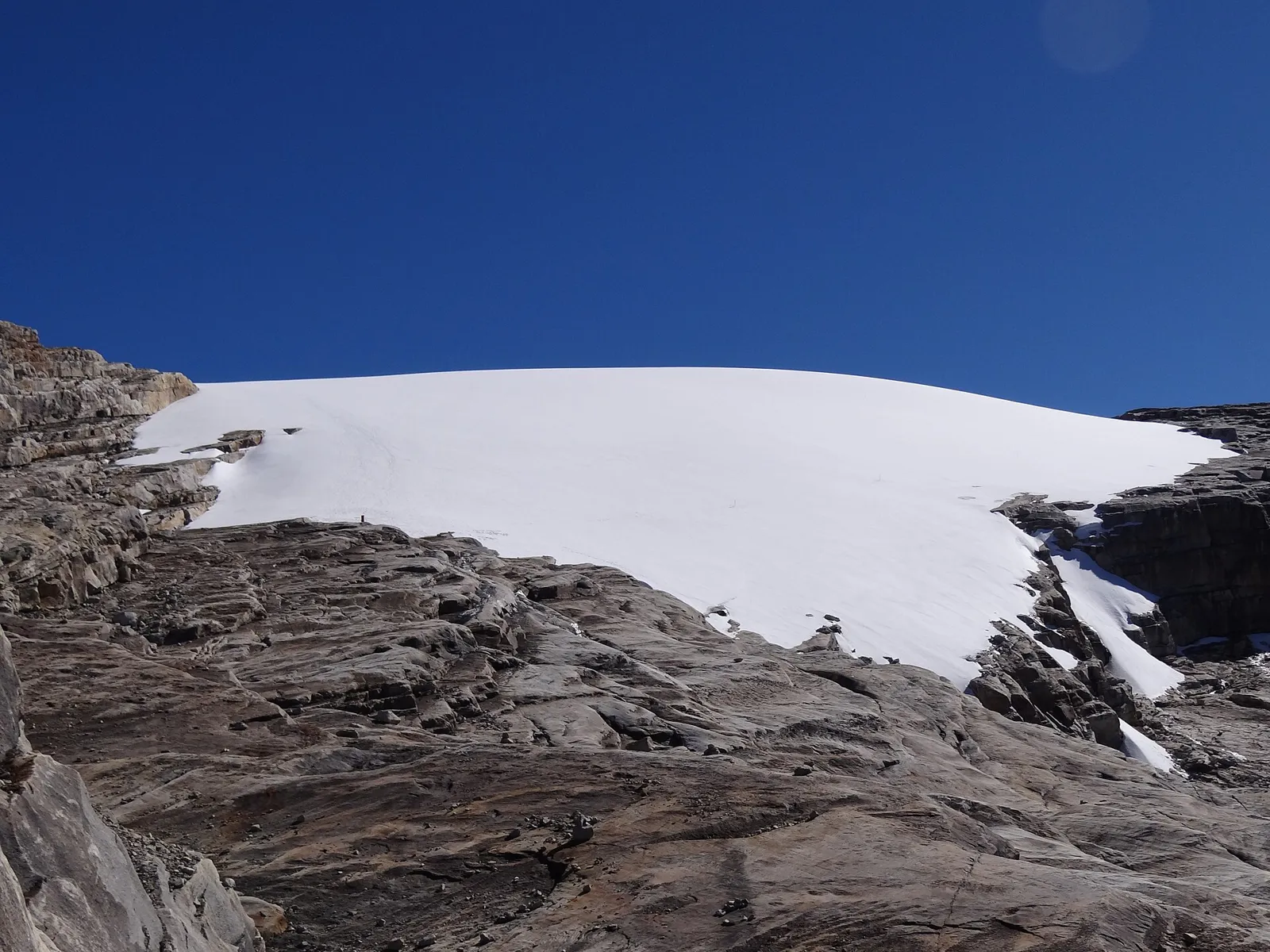 Borda do glaciar do Ritacuba Blanco no Parque El Cocuy, com rochas escuras em primeiro plano e céu azul