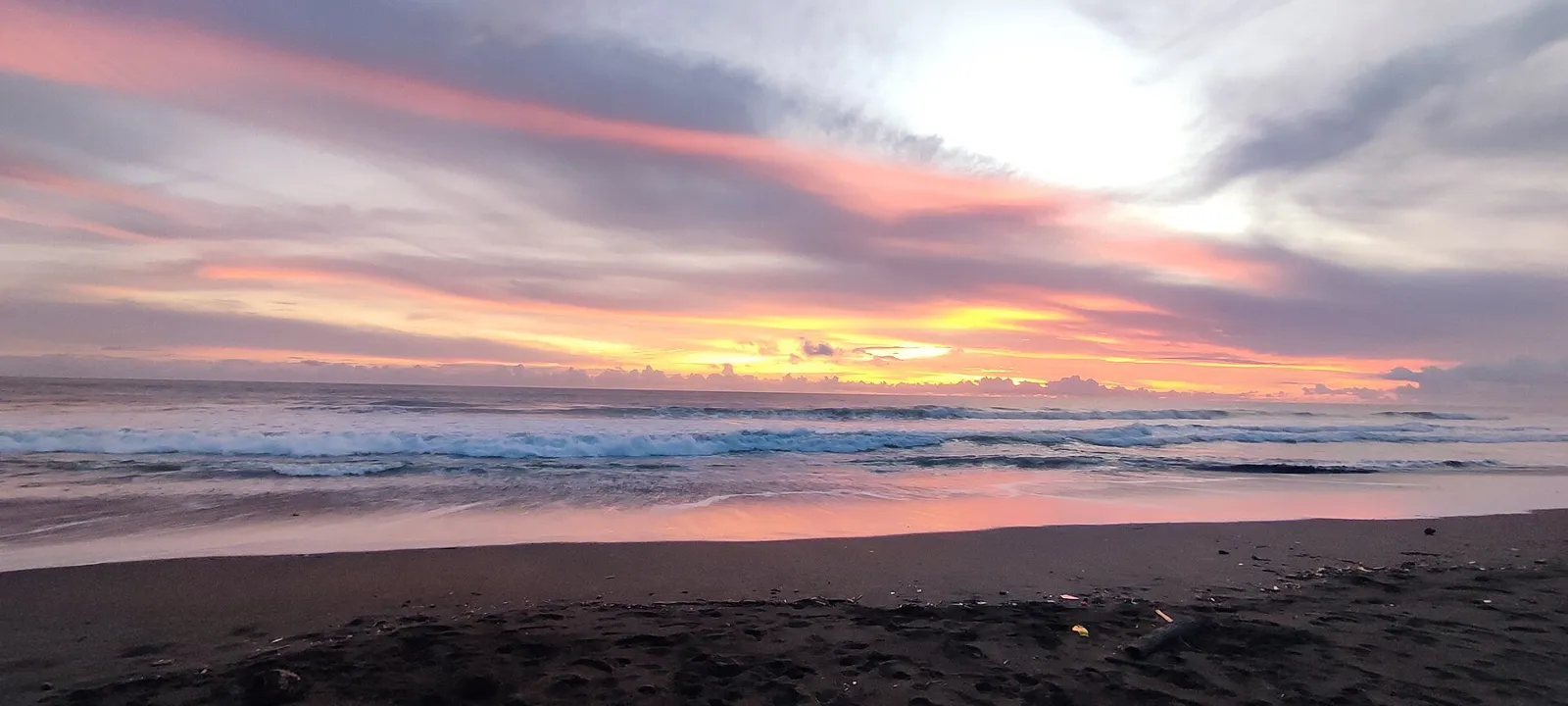 Pôr do sol com céu rosado sobre a praia de areia escura de Bahía Solano, no Pacífico colombiano