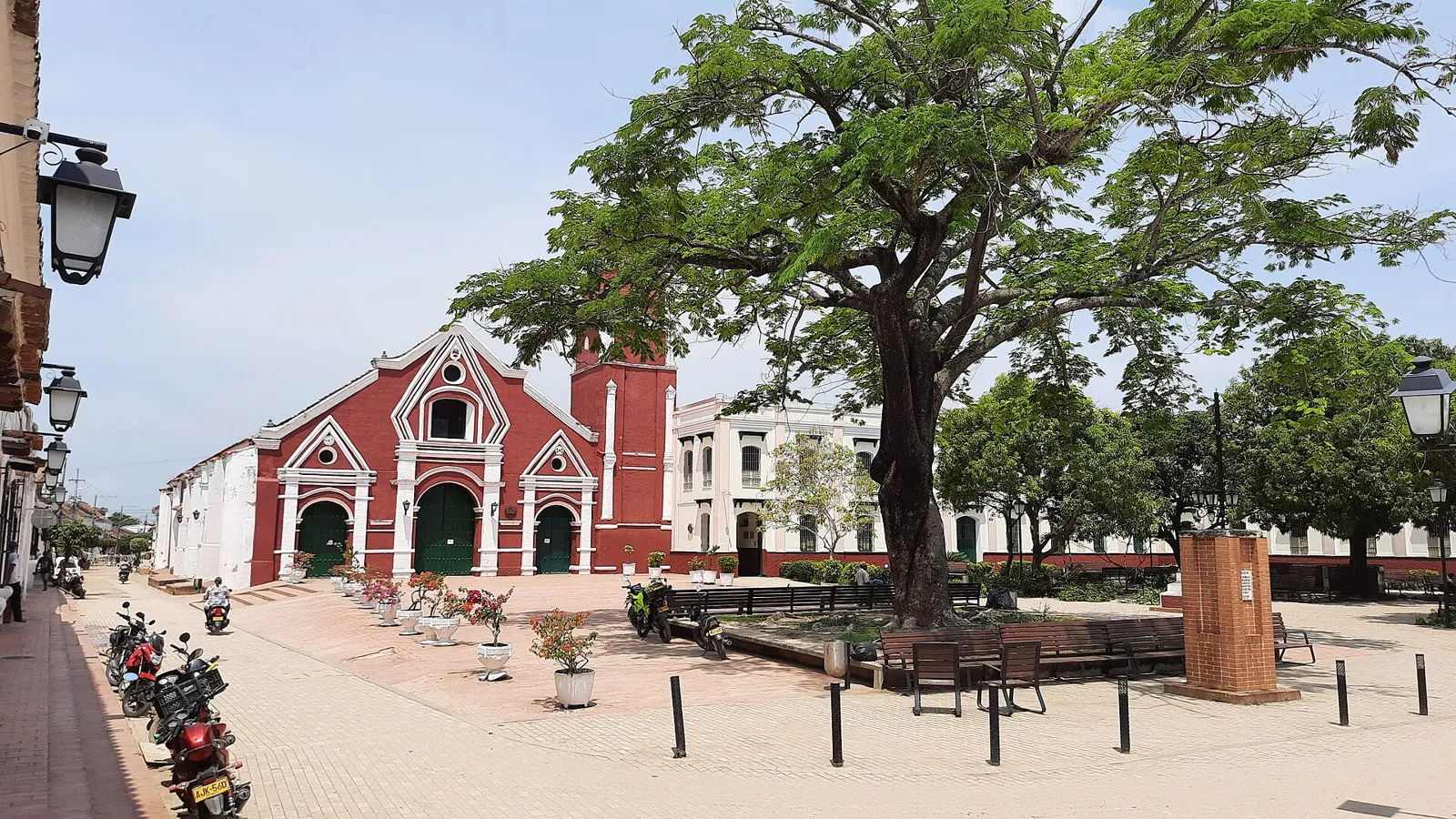 Praça de San Francisco em Mompox, com a igreja de fachada vermelha e branca, árvore grande e motos estacionadas