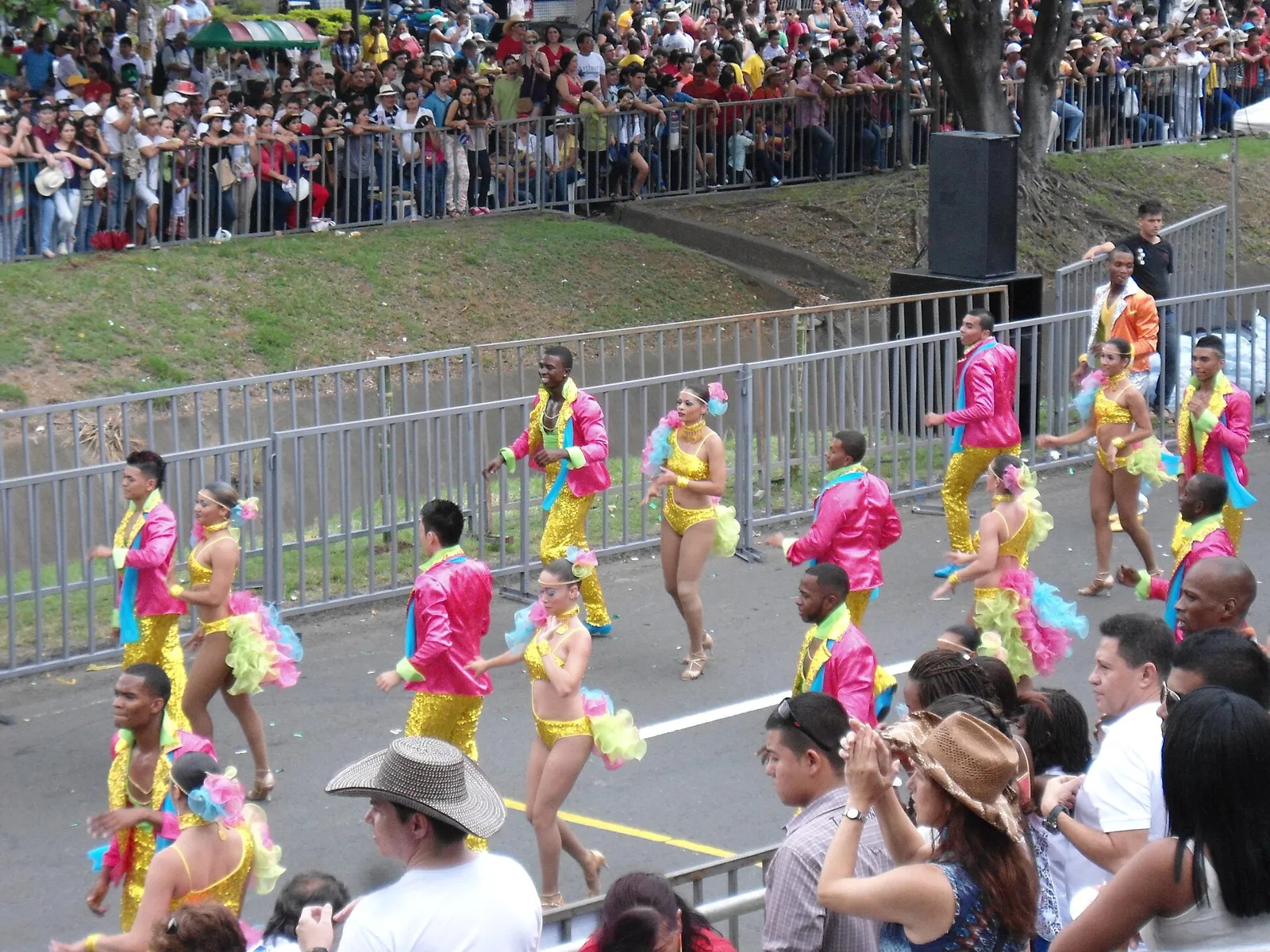 Bailarinos de salsa com figurinos coloridos desfilando no Salsódromo da Feria de Cali, com público nas grades