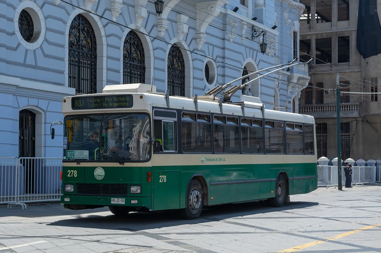 Trólebus verde e creme circulando na Plaza Sotomayor, em Valparaíso, diante do edifício histórico da Armada